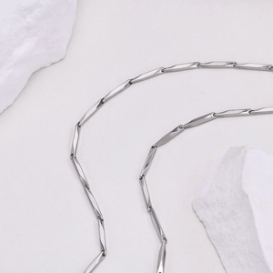Minimalist silver twist chain necklace detail on white stone texture background