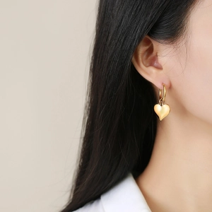 Gros plan d'un mannequin portant des boucles d'oreilles cœur dorées au fini satiné chic
