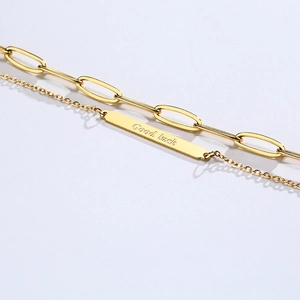 Detailed macro view of a gold double-layer chain bracelet with a Good Luck engraved metal plate