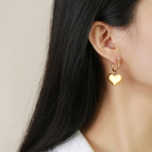 Gros plan d'une boucle d'oreille pendante cœur dorée avec finition miroir sur un mannequin