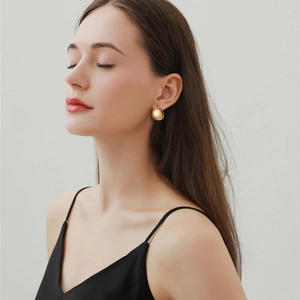 Nahaufnahme einer Frau mit glänzenden goldenen Kuppelohrringen im minimalistischen C-Design