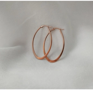 Macro detail of large rose gold oval hoop earrings with polished finish on silk fabric