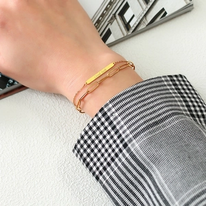 Close-up of gold double-layer bracelet with Good Luck tag on houndstooth background