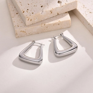 Polished silver U-shaped stainless steel earrings on a beige stone surface detail