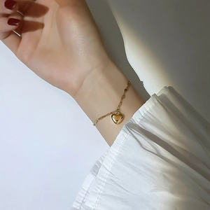 Detail of elegant gold heart pendant bracelet worn against white fabric background