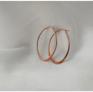 Detailed view of large rose gold teardrop hoop earrings on soft white fabric background