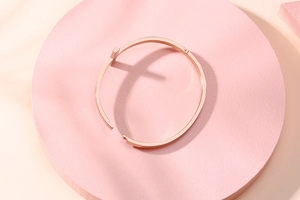Gros plan d'un bracelet jonc T-shape en acier inoxydable or rose sur socle rose