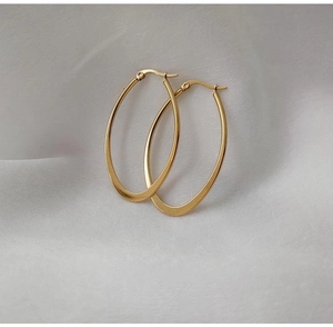 Detailed view of polished gold oval hoop earrings on soft grey silk fabric surface