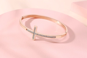 Détail du bracelet croix en or rose avec strass brillants sur support rose