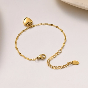 Elegant gold heart charm bracelet with K18 engraving on a minimalist textured surface