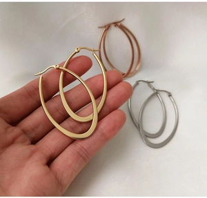 Close-up of high-polished gold, rose gold, and silver oval hoop earrings on white fabric