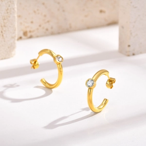 Detail of 18K gold-plated C-shaped earrings with round zircon on stone background