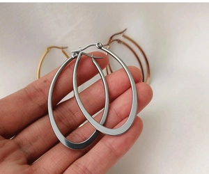 Close-up of large oval hoop earrings in gold, silver, and rose gold finishes held by hand