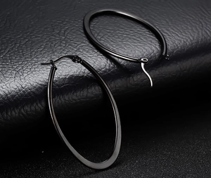 Close-up of black oval hoop earrings with smooth metal finish on a textured surface
