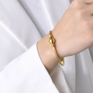 Dettaglio di un bracciale a cavo ritorto oro minimalista con una perla di metallo lucido