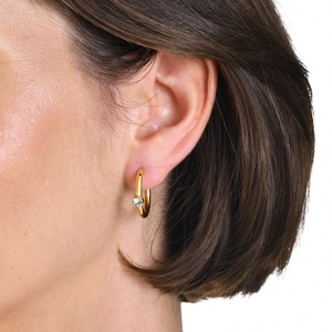 Close-up of a 18K gold plated C-shaped hoop earring with a sparkling zircon on a model