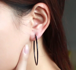 Close-up of model wearing large matte black round hoop earrings in minimalist style