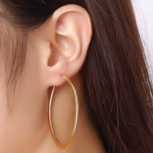 Close-up of a model wearing large polished gold hoop earrings with a mirror finish