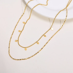 Détail macro d'un collier double épaisseur doré avec pendentif losange sur plat
