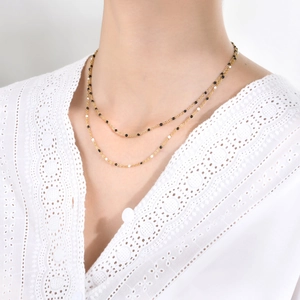 Detail of layered gold chain necklace with black and white beads on a model collar