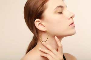 Close-up of golden Mobius twist hoop earrings on a model showing the texture