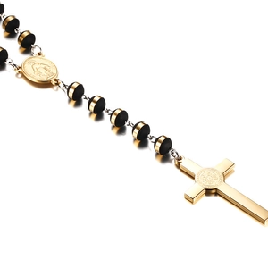 Golden Saint Benedict cross necklace with black beads and religious medal on grey surface