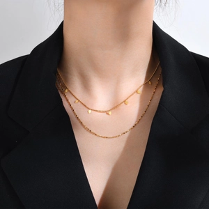 Détail d'un collier double épaisseur doré avec pendentifs losanges sur une veste noire