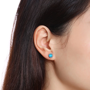Close-up of a round turquoise stud earring with silver metal setting on a model ear