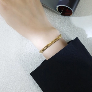 Detail of layered gold snake chain bracelet worn on wrist with black blazer