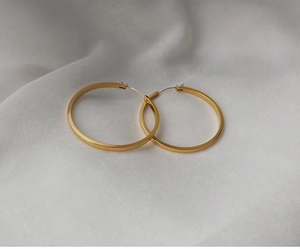 Détail de grandes créoles plaquées or 18 carats avec finition métal lisse sur fond soie