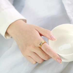 Close-up of 18k gold-plated ring with square green zircon worn on a hand holding a cup