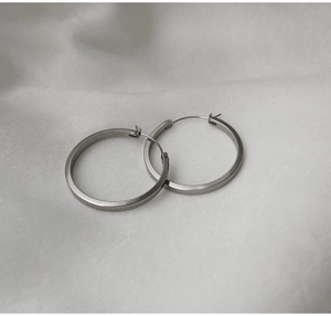 Gros plan de boucles d'oreilles créoles argentées sur tissu en soie blanche et ombre
