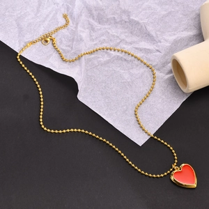 Golden bead chain necklace featuring a red enamel heart locket pendant on a stone display