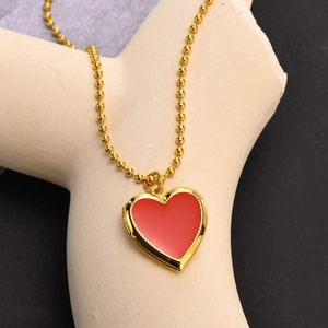 Detail of a golden ball chain with a red heart locket pendant on a display stand