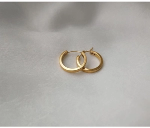 Détail de créoles plaquées or 18 carats sur un élégant fond en tissu de soie blanc
