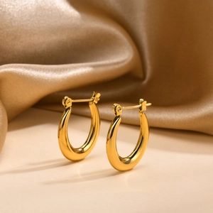 Close-up of gold U-shaped earrings with polished finish on champagne silk fabric