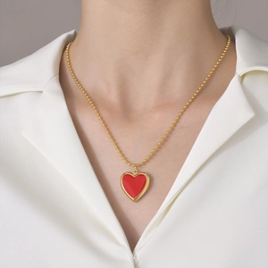 Golden bead chain necklace featuring a red enamel heart locket on a white silk shirt