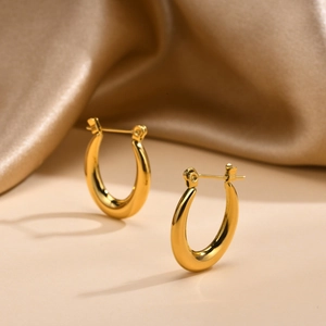 Detail of gold U-shaped hoop earrings with a polished finish on soft silk background