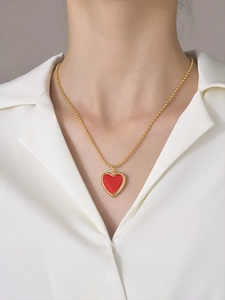 Elegant gold beaded chain necklace with a red heart-shaped enamel locket pendant on a model