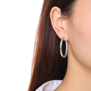 Gros plan d'une boucle d'oreille créole argentée polie portée par un mannequin