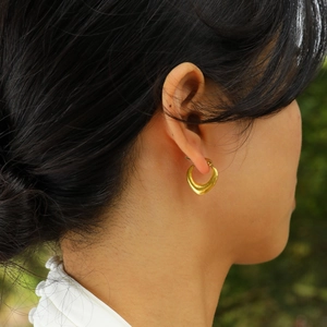 Nahaufnahme eleganter 18K vergoldeter U-Ohrringe, getragen von einem Model im Freien