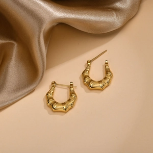 Detail of gold bamboo textured U-shape earrings on elegant silk background decor