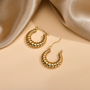 Detail of gold U-shaped hoop earrings with textured croissant pattern and glossy finish