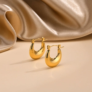 Close-up of golden U-shaped hoop earrings on elegant champagne satin fabric background