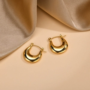 Detail of gold U-shaped chunky hoop earrings on elegant champagne silk fabric