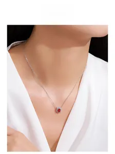Close-up of elegant oval ruby pendant necklace with halo diamond setting on a silver chain
