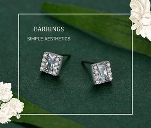 Macro detail of silver square stud earrings with rectangular zircon on green background