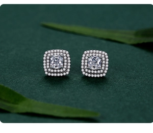 Macro shot of silver square halo earrings with cushion-cut gems on green silk