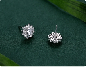 Vue macro des boucles d'oreilles tournesol en argent et zircons sur fond vert texture
