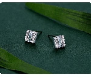 Macro detail of silver square stud earrings with pave crystals on deep green background